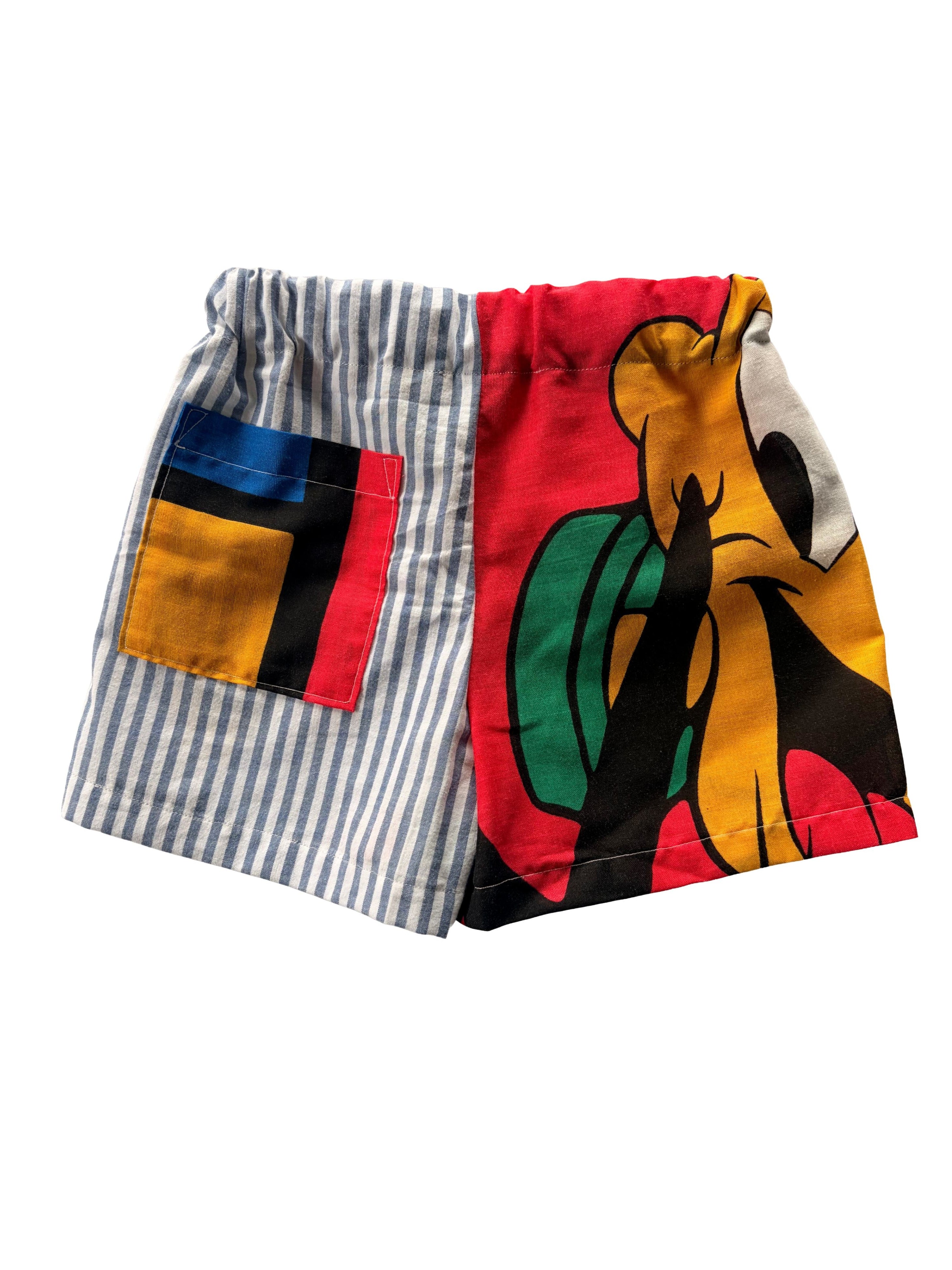 Handcrafted toddler shorts featuring blue-and-white striped fabric with a patch pocket on one side and a bold Pluto character print on the other.